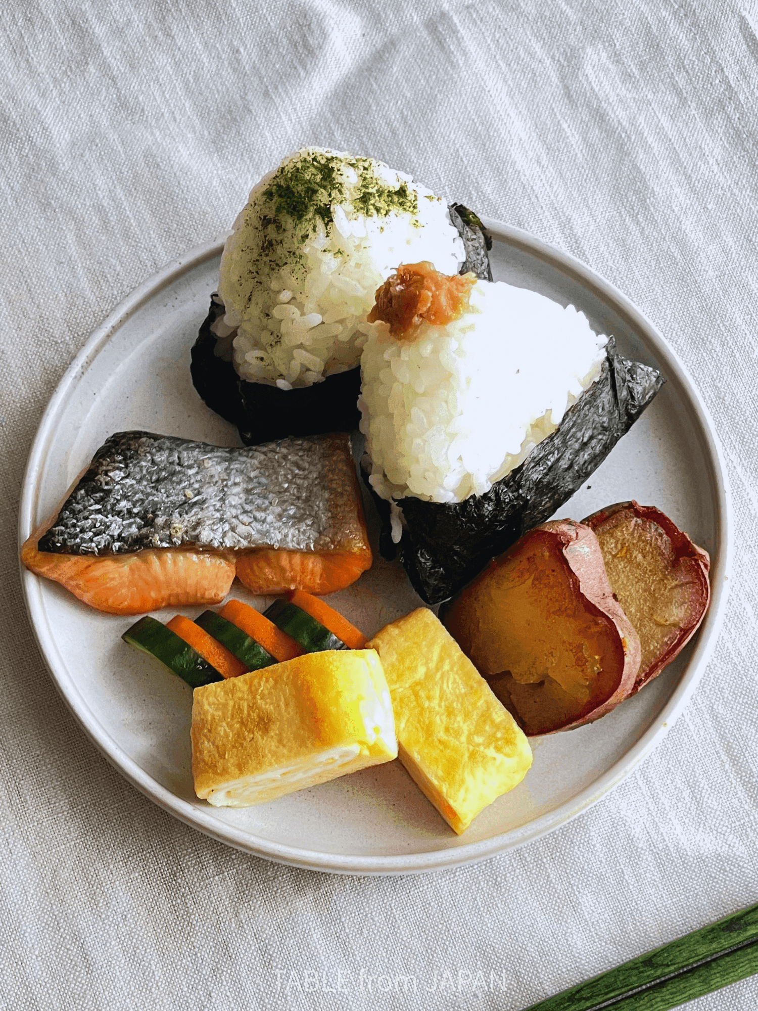 One plate of Japanese home cooking with rice balls, salmon, tamagoyaki and vegetables
