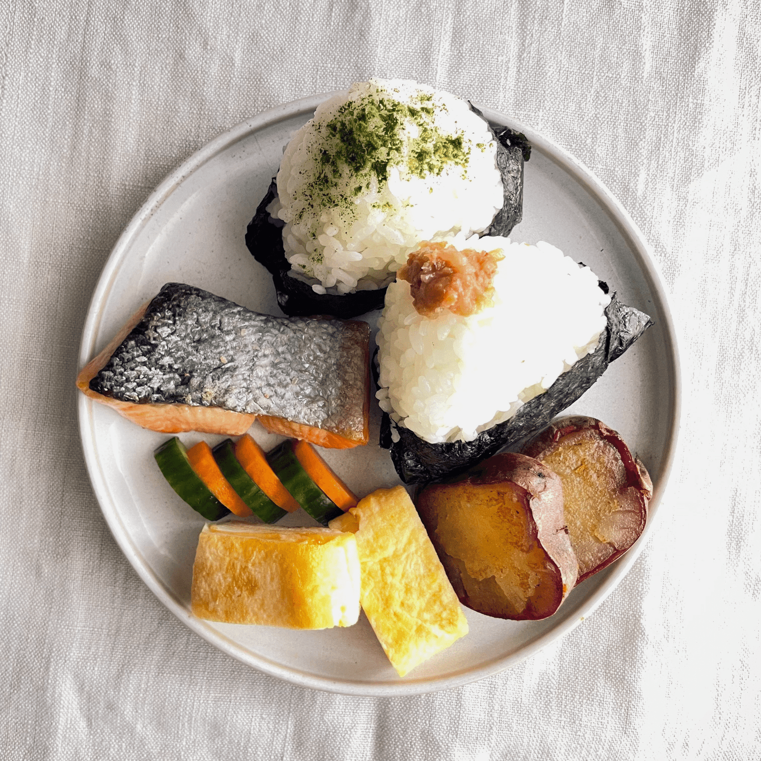 One plate of Japanese home cooking with rice balls, salmon, tamagoyaki and vegetables